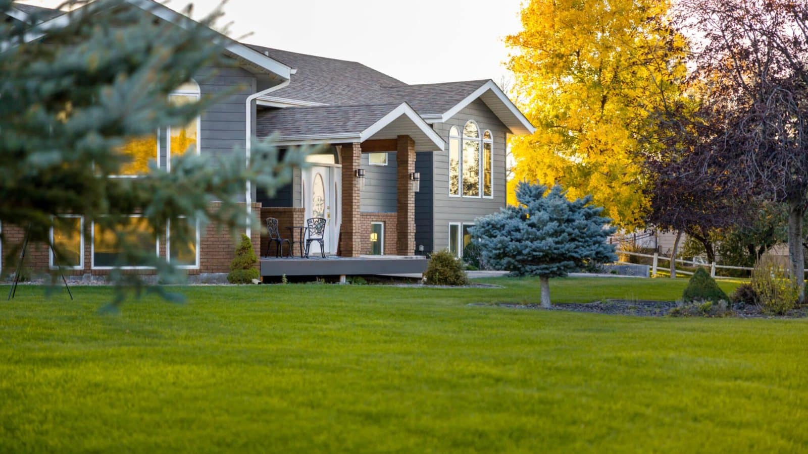 Two-story home with a green lawn and fall trees